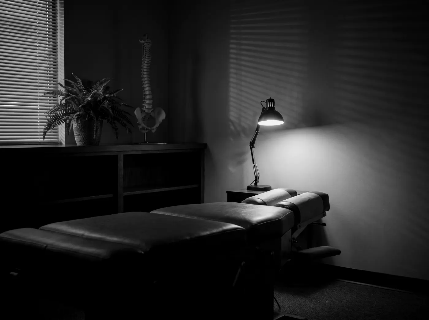 A quiet chiropractic room at dusk with the adjustment table under a lamp