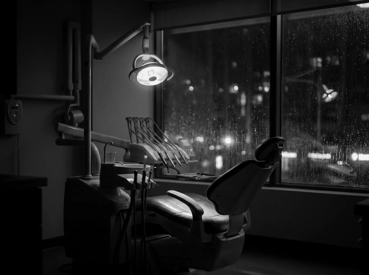 A dental treatment room after hours, the chair lit by a single lamp