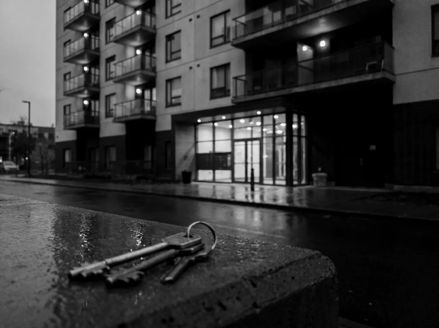 Keys resting on a ledge outside a lit apartment building at blue hour