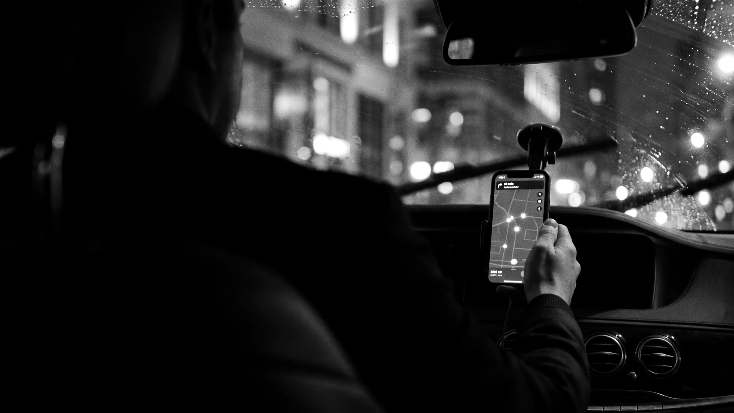 A driver at night checking a map on a phone mounted in the car